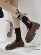 Legs of a person wearing brown knee-high ribbed socks with a plush bunny applique and brown chunky sole loafers.