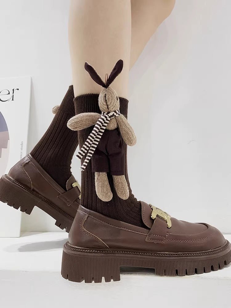 A person wearing brown knee-high ribbed socks with a plush bunny applique and brown chunky sole loafers.