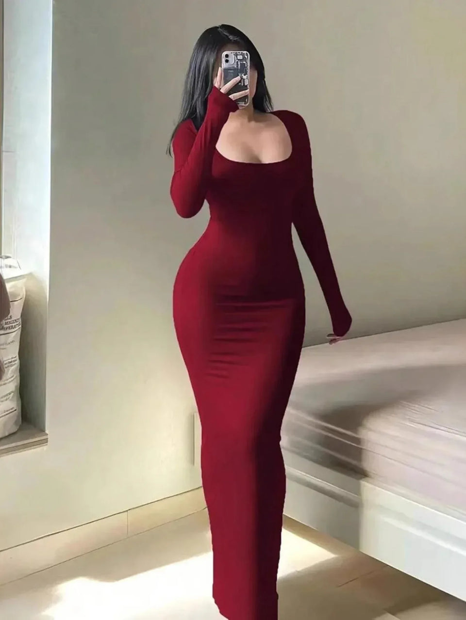 Woman wearing a long-sleeved, scoop-neck, form-fitting, floor-length mermaid silhouette dress in dark red, posing in a room. Main image