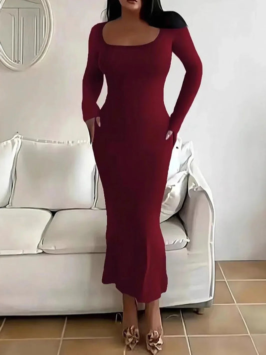 Woman wearing a long-sleeved, scoop-neck, form-fitting, floor-length mermaid silhouette dress in dark red, standing in a living room.