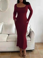 Woman wearing a long-sleeved, scoop-neck, form-fitting, floor-length mermaid silhouette dress in dark red, standing in a living room.
