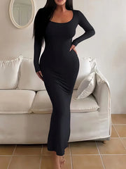 Woman wearing a long-sleeved, scoop-neck, form-fitting, floor-length mermaid silhouette dress in black, standing in a living room.