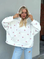 Close-up of a woman wearing an oversized white hooded sweatshirt with a pink bow print, adjusting the hood.