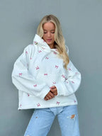 Woman in an oversized white hooded sweatshirt with a pink bow print, paired with distressed light-wash denim jeans.
