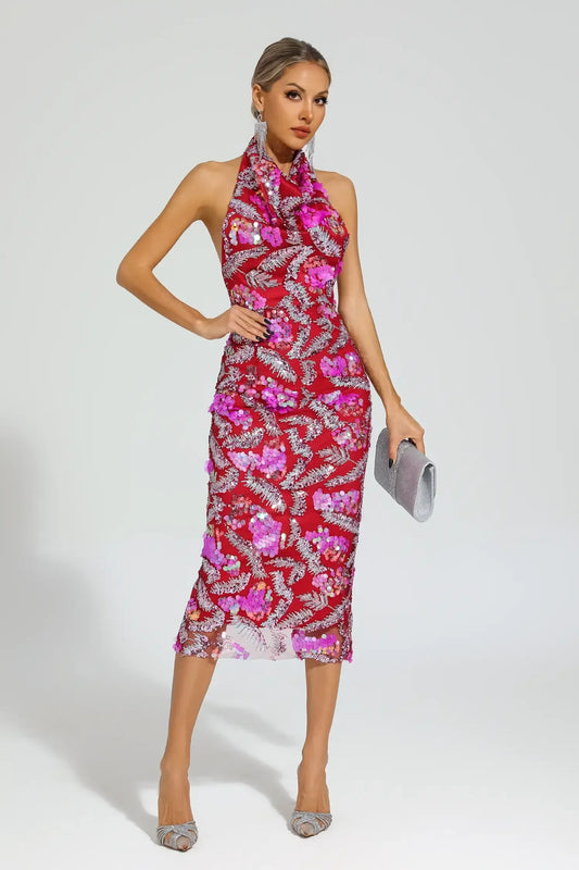 Woman in a red sequined halter midi dress with floral appliques, hands on hips.