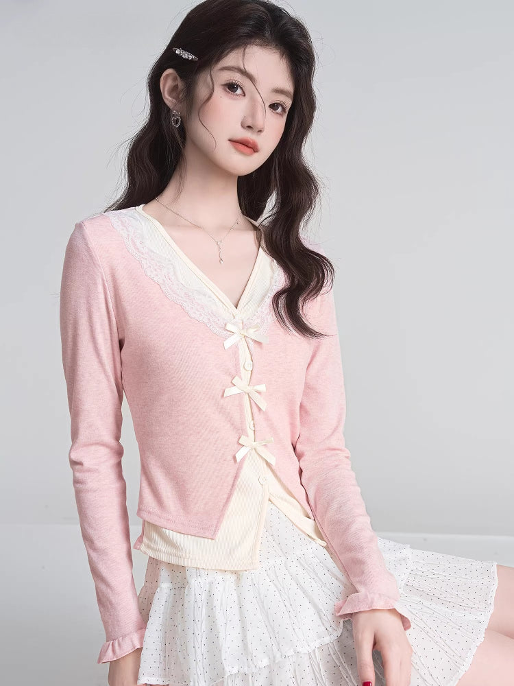 Woman posing in a pink V-neck knit cardigan with lace trim and bow closures, layered over a cream top and white polka dot skirt.