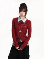 Close-up of the woman's torso showing the red cable knit cardigan with a light blue collared shirt and gold cross necklace.