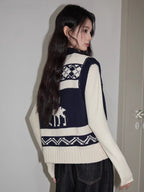 Rear view of a woman wearing a navy and cream floral and geometric knit vest over a cream long-sleeve top and dark wash wide-leg jeans.