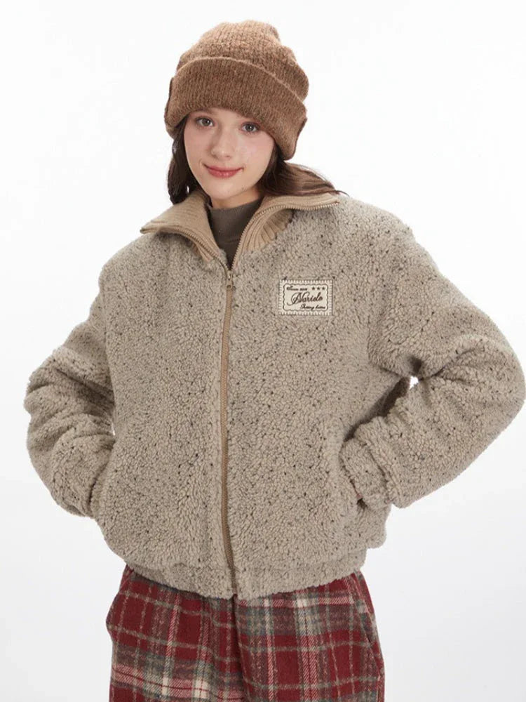 Front view of a model wearing a beige fuzzy bomber jacket and red plaid pants, with hands in pockets.
