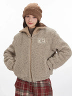 Front view of a model wearing a beige fuzzy bomber jacket and red plaid pants, with hands in pockets.