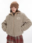 Front view of a model wearing a beige fuzzy bomber jacket and red plaid pants, with hands in pockets.