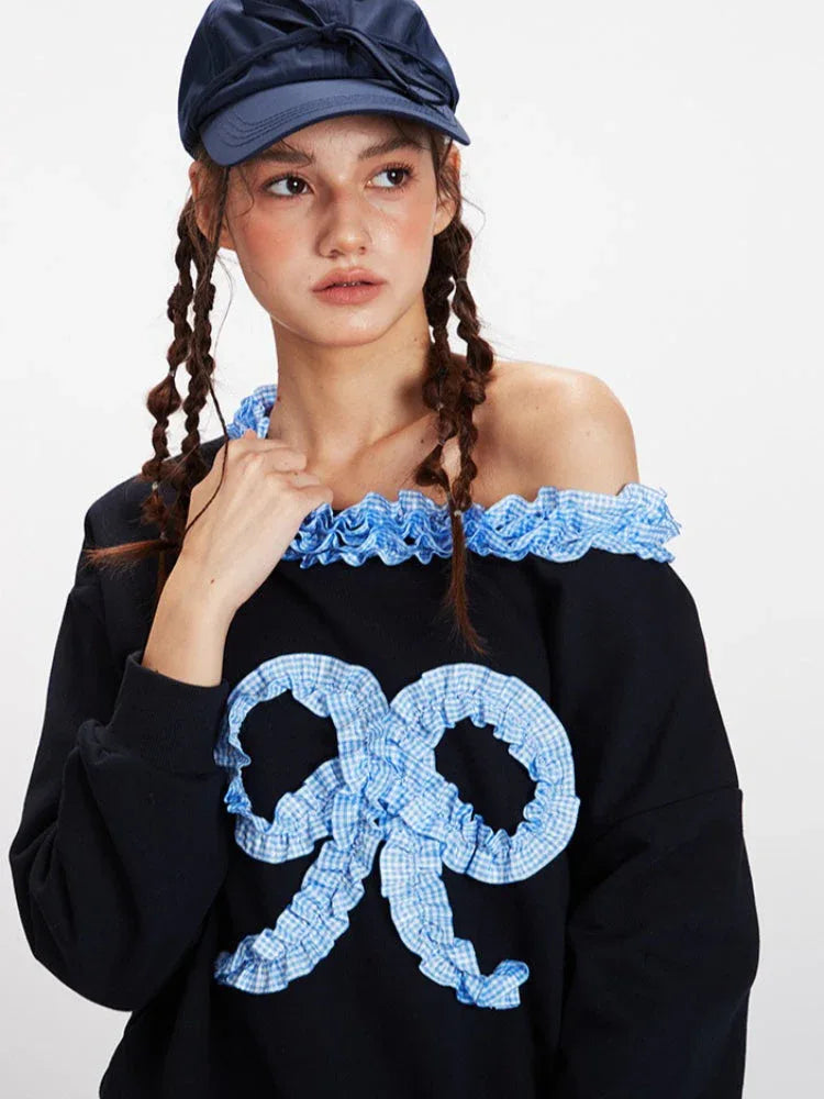 Detailed view of the neckline and bow on the black sweatshirt, showing the ruffled blue trim and the checkered texture of the bow.