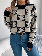 Front view of a woman wearing a black and white ghost print checkerboard knit sweater with blue jeans and a black belt.