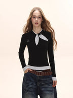 Model from the chest up wearing a black long-sleeve top with a white polka dot scarf detail and white polka dot cuffs, with a small embroidered logo on the chest.