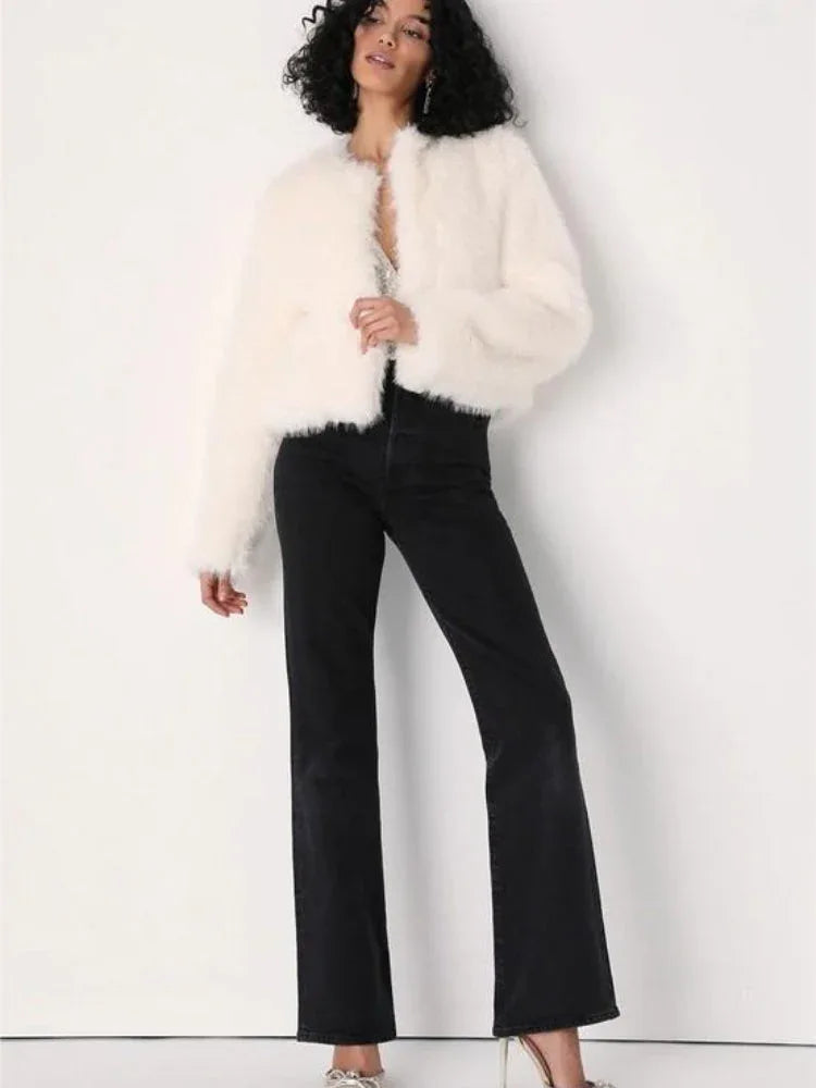 Full-body shot of a woman wearing a white faux fur jacket, sparkly top, and black flared jeans.