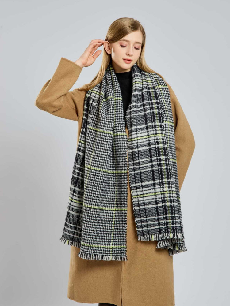 Woman in a tan coat adjusting her large houndstooth and plaid scarf
