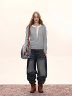 Woman wearing a light grey knit henley sweater with a white collar, dark wash wide-leg jeans, brown boots, and a denim shoulder bag.