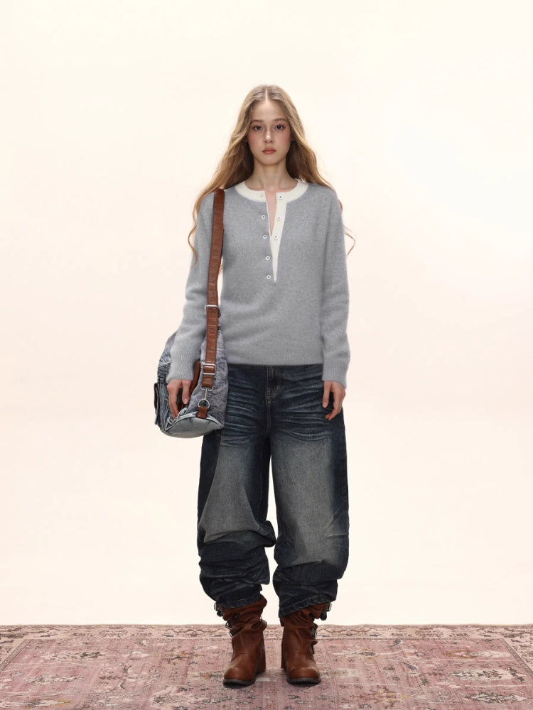 Woman wearing a light grey knit henley sweater with a white collar, dark wash wide-leg jeans, brown boots, and a denim shoulder bag.