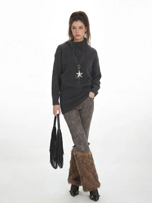 Woman in a charcoal grey oversized turtleneck knit tunic, patterned leggings, and brown furry leg warmers, holding a black fringed handbag.