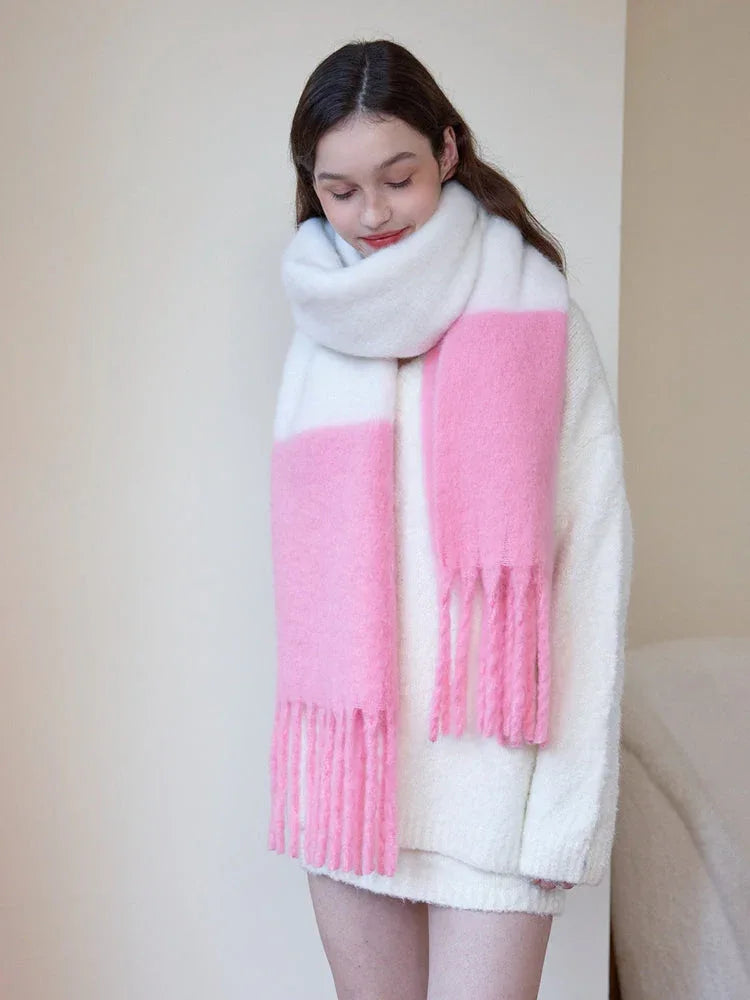 Woman wearing a white sweater and a white and pink two-tone fuzzy knit scarf with fringe trim, looking down.