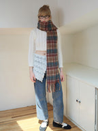 Full body shot of a model wearing a white cable knit cropped sweater, blue denim jeans, a plaid scarf, crochet overlay, and glasses, standing.