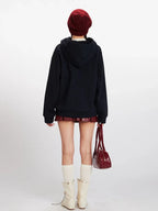 Back view of a woman wearing a dark blue hooded cardigan with colorful fruit buttons, a red beanie, a red faux leather pleated skirt, white knee-high socks, and cream-colored boots.