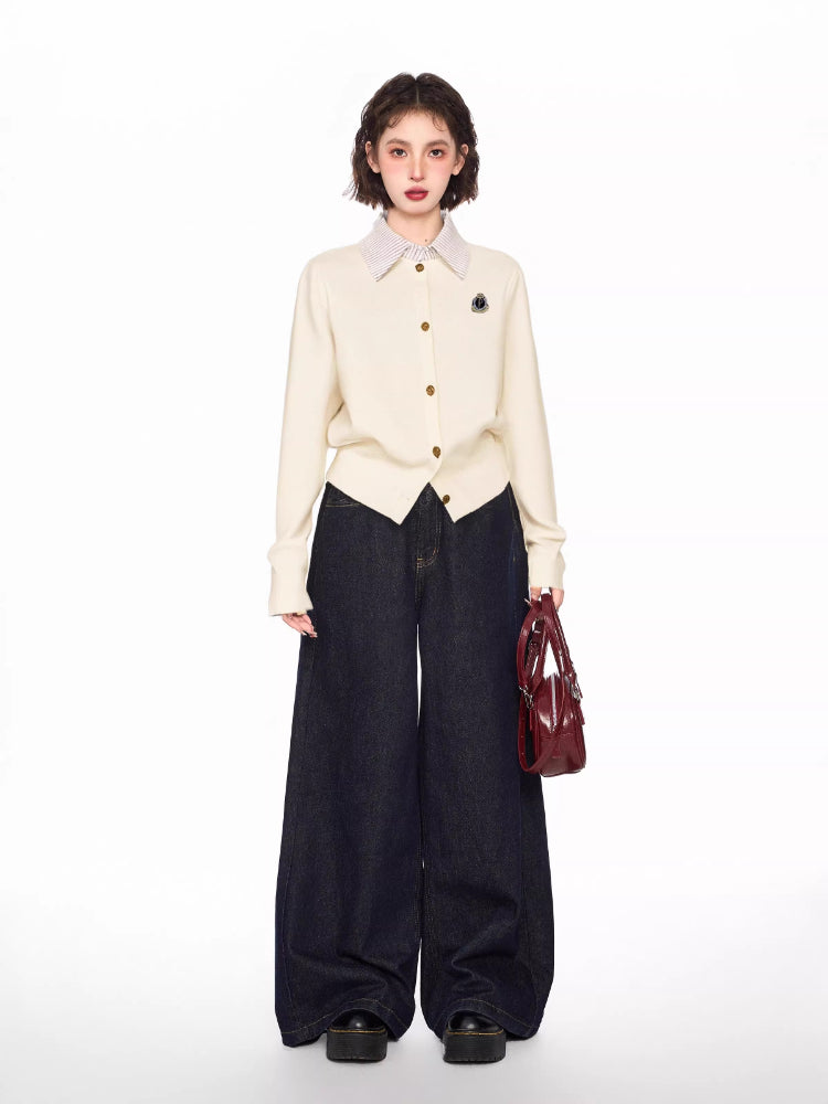 Woman wearing a cream-colored knit cardigan over a striped collared shirt, paired with dark wash wide-leg jeans and a burgundy handbag.