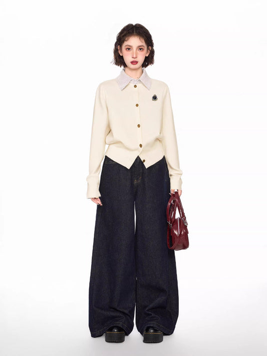 Woman wearing a cream-colored knit cardigan over a striped collared shirt, paired with dark wash wide-leg jeans and a burgundy handbag.