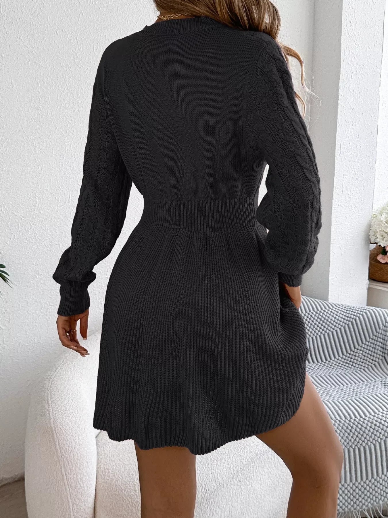 Rear view of a woman wearing a black long-sleeved knit dress with cable knit detailing on the bodice and an A-line skirt.