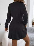 Rear view of a woman wearing a black long-sleeved knit dress with cable knit detailing on the bodice and an A-line skirt.