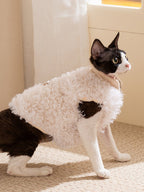 Side view of a black and white cat wearing a white sherpa fleece vest.
