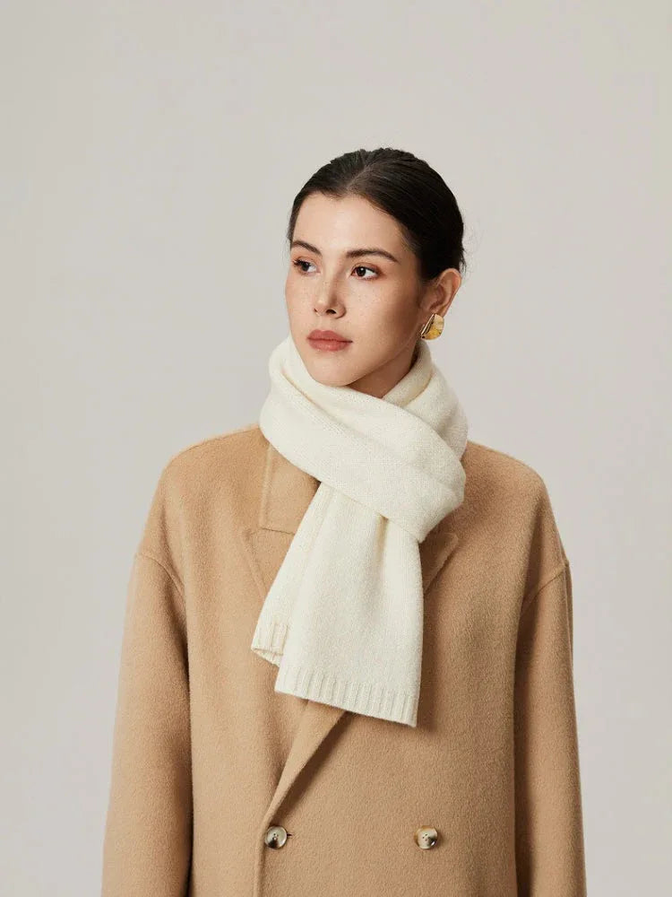 Woman wearing an ivory knit scarf and a tan coat.
