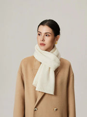 Woman wearing an ivory knit scarf and a tan coat.