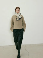 Woman walking towards the camera in a beige textured coat, cream scarf with black trim, and black pants
