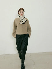 Woman walking towards the camera in a beige textured coat, cream scarf with black trim, and black pants