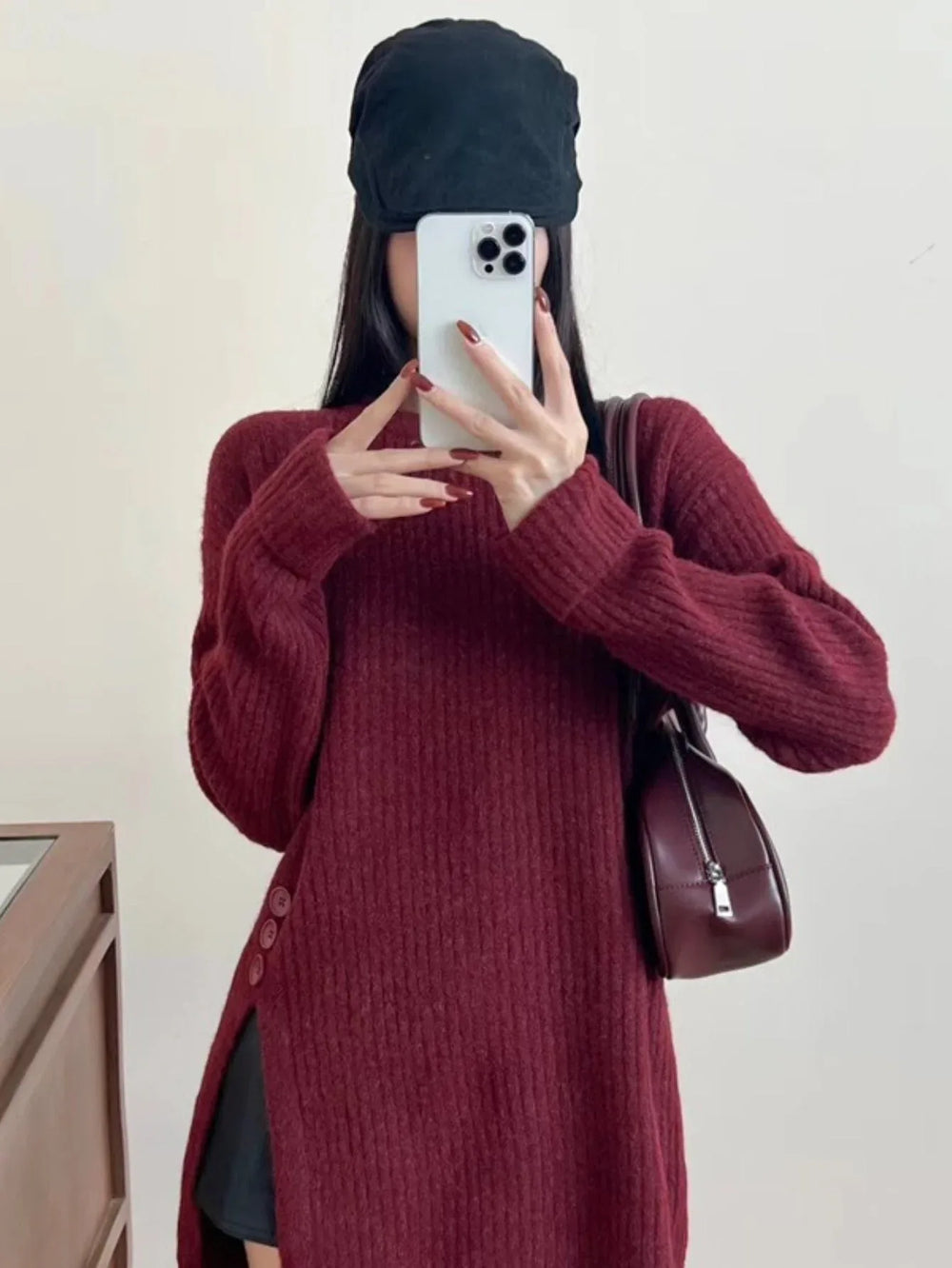 Woman wearing a burgundy ribbed knit longline tunic with side slits and buttons, black shorts, and brown boots, with a black baseball cap on.