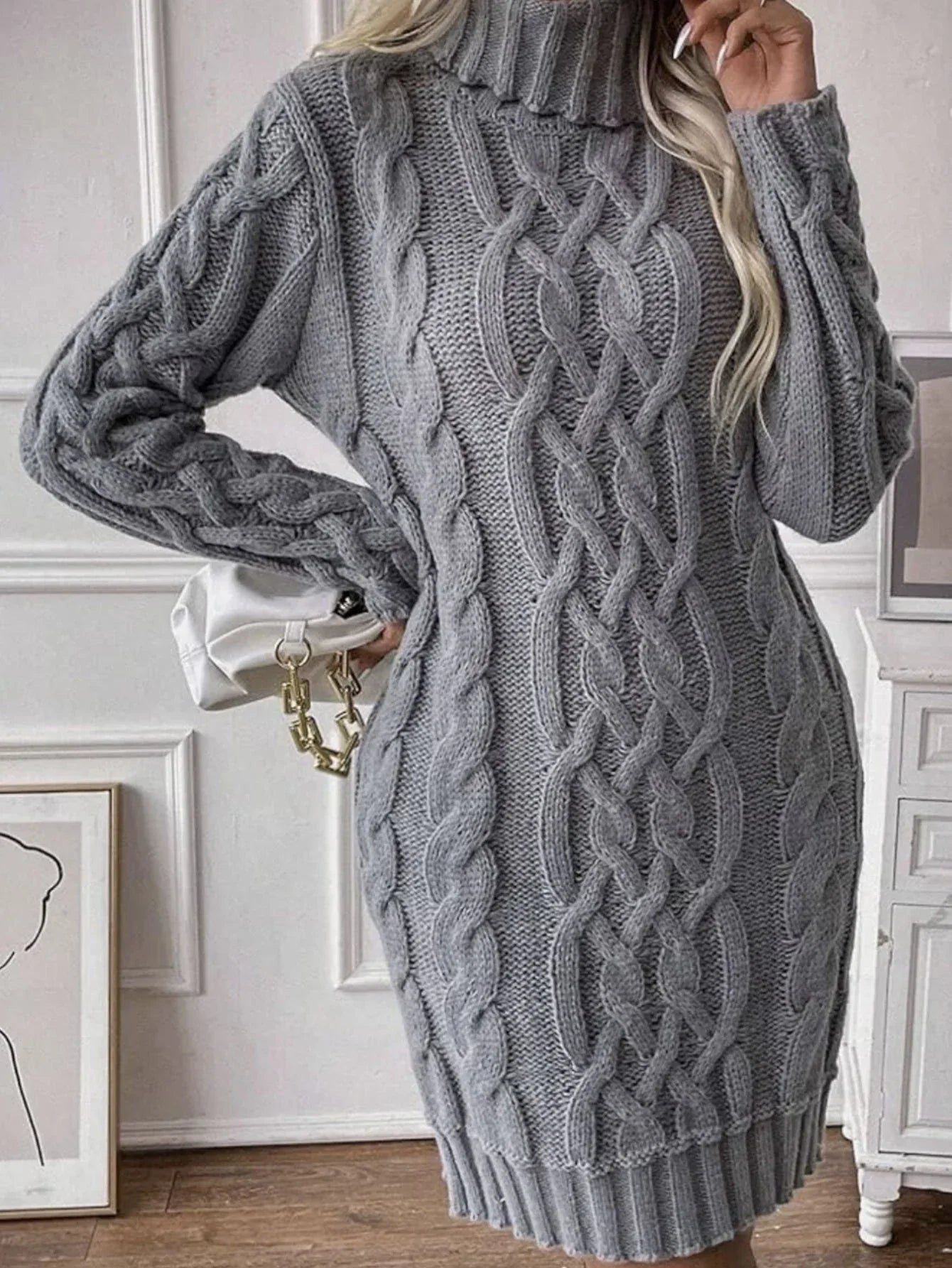 Close-up of a woman wearing a grey cable knit turtleneck mini dress and holding a white handbag.