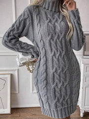 Close-up of a woman wearing a grey cable knit turtleneck mini dress and holding a white handbag.