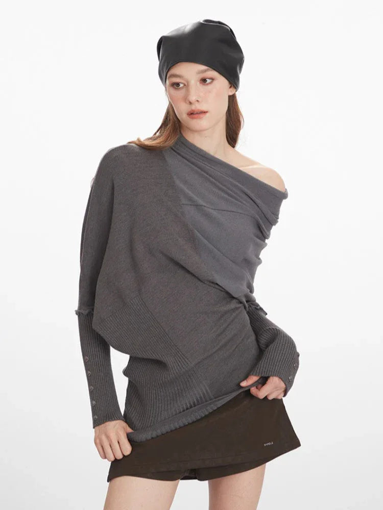 Woman showing the draped detailing and asymmetry of her grey knit sweater.