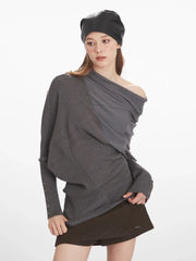 Woman showing the draped detailing and asymmetry of her grey knit sweater.