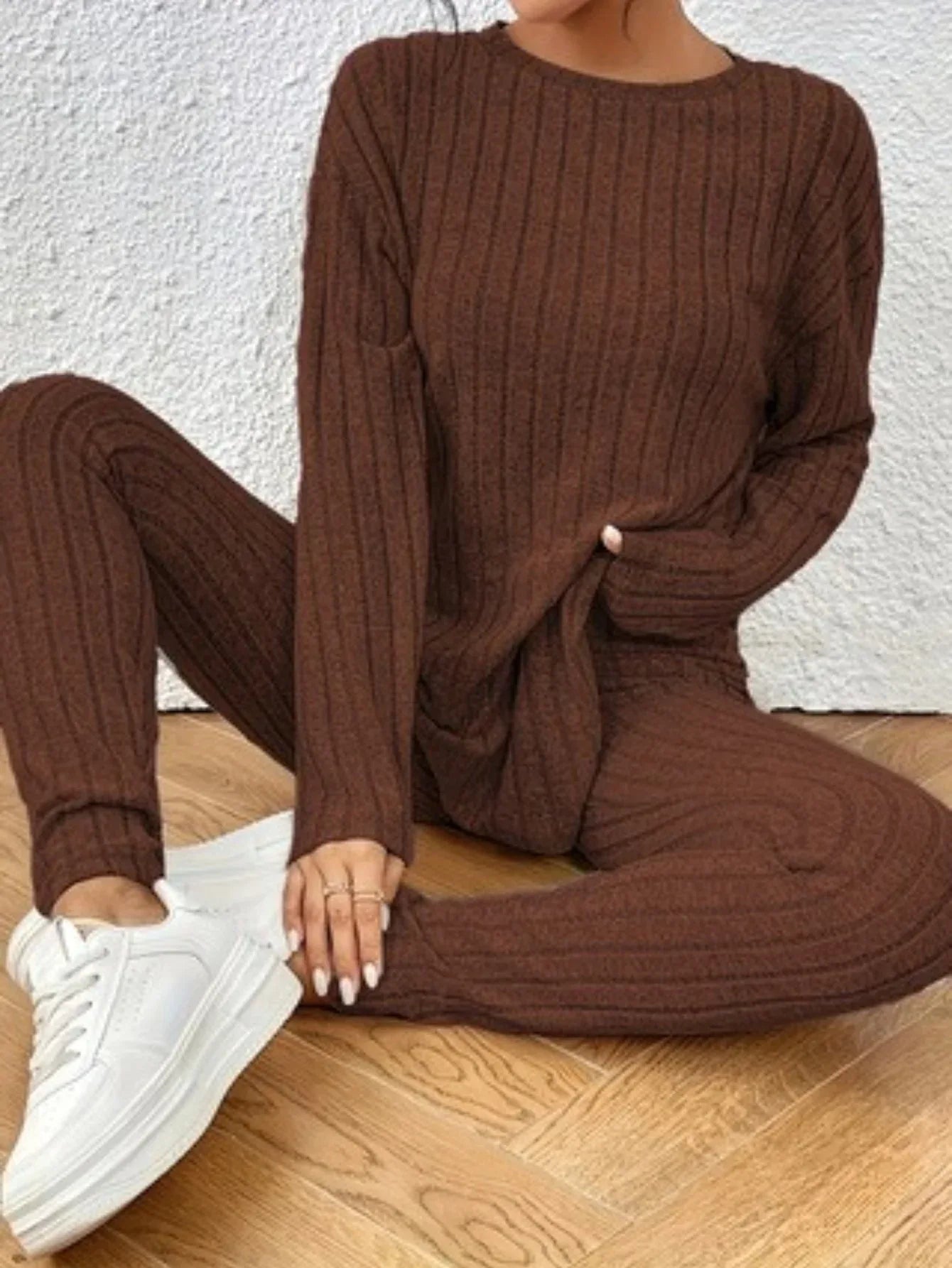 Close-up of a woman's legs and torso in a brown ribbed knit loungewear set, sitting on the floor.