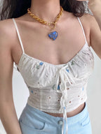 Detail of the white eyelet fabric and blue floral embroidery on a cropped camisole top.