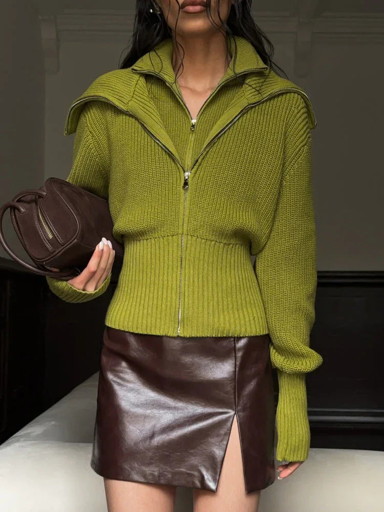 Model holding a brown handbag while wearing a lime green zip-up knit sweater and a brown leather mini skirt.