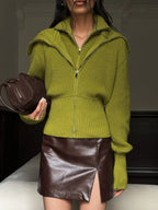 Model holding a brown handbag while wearing a lime green zip-up knit sweater and a brown leather mini skirt.