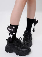 A person is wearing black socks with cat appliques and black platform shoes.