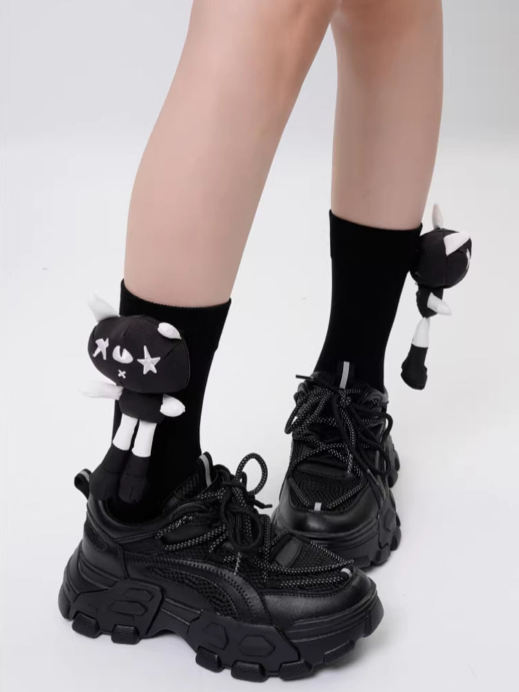 A person is wearing black socks with cat appliques and black platform shoes.