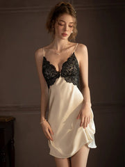 Woman wearing a cream-colored satin chemise with black lace trim, standing against a dark wall.
