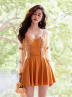 Woman in a mustard yellow one-piece swimsuit with sheer puff sleeves and embroidered trim, standing outdoors with a bouquet of roses.