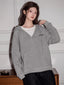 Woman wearing a grey V-neck oversized hoodie over a white t-shirt, standing in front of a white wall.