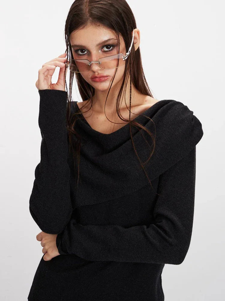 Close-up of a woman's face and upper body, highlighting the asymmetrical knit sweater and sunglasses.